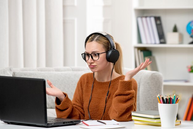 手を振ってコンピュータで勉強している眼鏡とオレンジ色のセーターの学生オンライン若いかわいい女の子