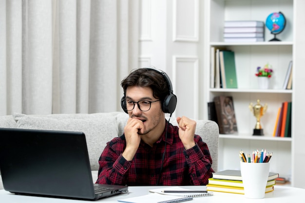 Student online young guy in checked shirt with glasses studying on computer biting finger