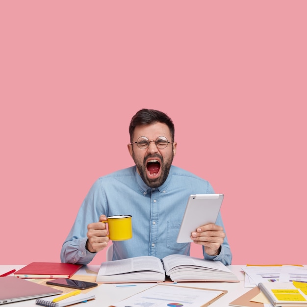 Student sitting at desk with documents holding cup and tablet