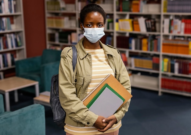 Foto gratuita studente che indossa una maschera facciale in biblioteca