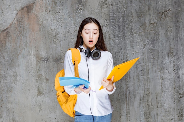 Student with backpack and headphones books in her hand looking shocked. High quality photo