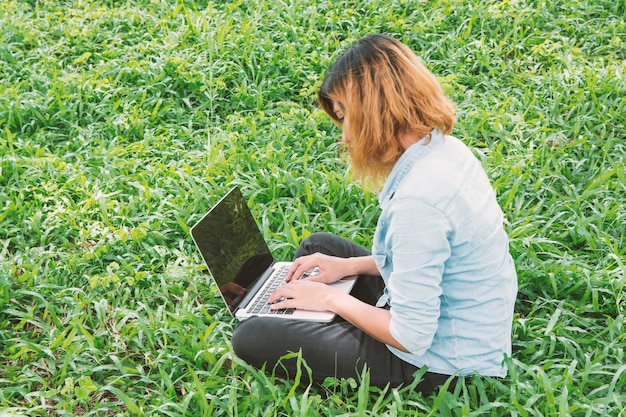 Foto gratuita studente con laptop, seduta sull'erba