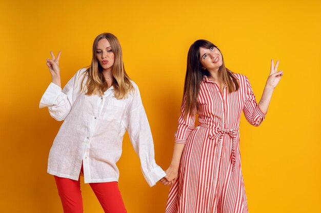 Studio bright positive portrait of two sisters woman having fun, color matching clothes, yellow  background. Cute emotions.