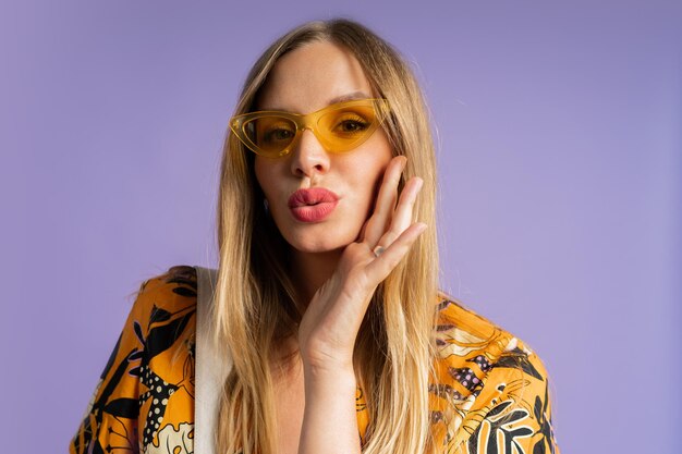 Studio close up fashion portrait of pretty blond woman in stylish top and linen shorts posing on purple background