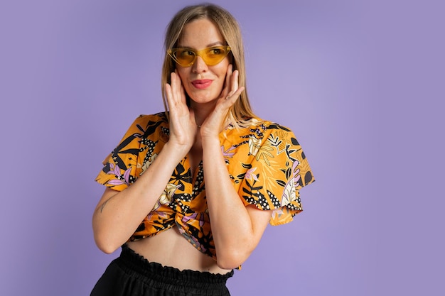 Studio close up fashion portrait of pretty blond woman in stylish top and linen shorts posing on purple background