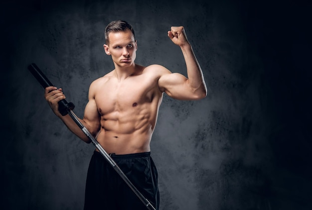 Studio image of shirtless muscular male holds barbell over grey vignette background.