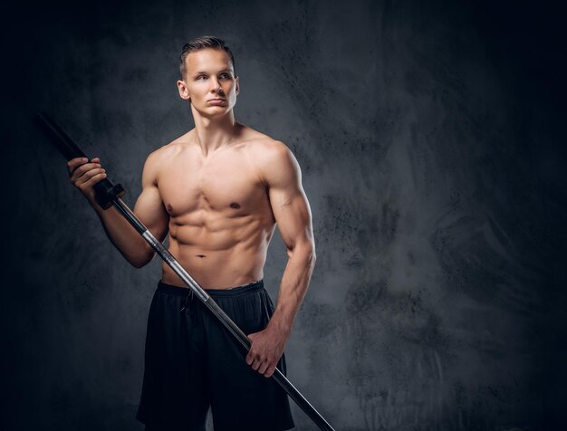 上半身裸の筋肉質の男性のスタジオ画像は、灰色のビネットの背景の上にバーベルを保持しています。