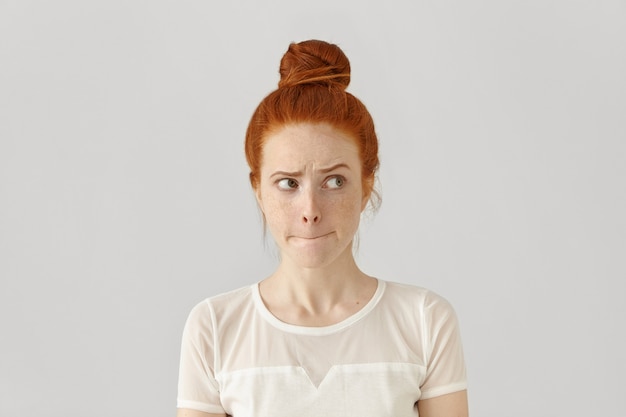 Free photo studio isolated shot of doubting confused cute young redhead freckled female looking sideways