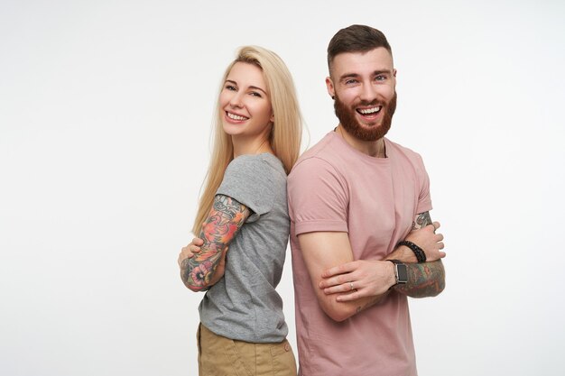 Studio photo of lovely glad couple keeping hands crossed on their chests and laughing happily while looking at camera  standing over white background