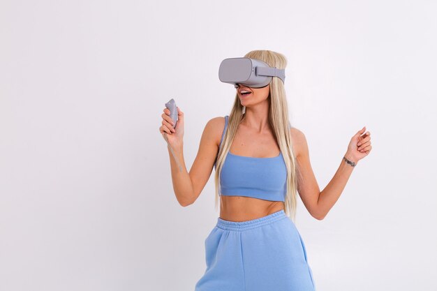 Studio photo of a young attractive woman in a warm blue fashionable suit wearing virtual reality glasses on a white