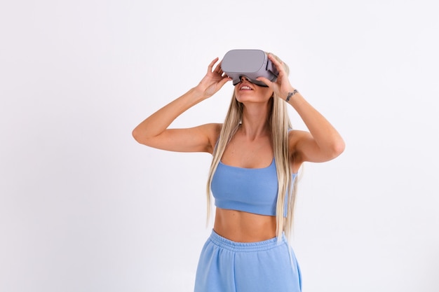 Studio photo of a young attractive woman in a warm blue fashionable suit wearing virtual reality glasses on a white