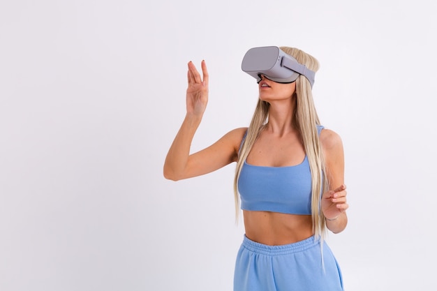 Studio photo of a young attractive woman in a warm blue fashionable suit wearing virtual reality glasses on a white