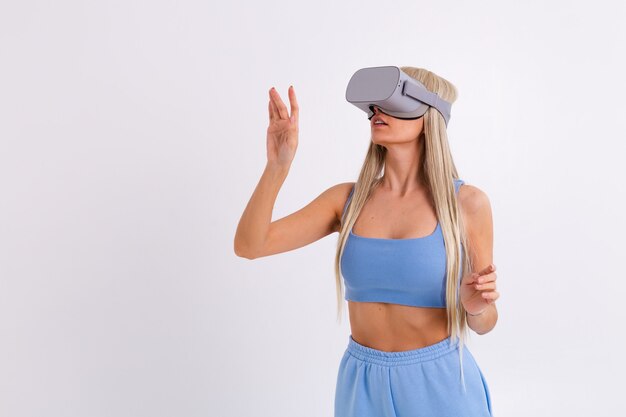 Студийное фото молодой привлекательной женщины в теплом синем модном костюме в очках виртуальной реальности на белом