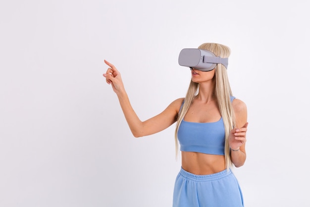 Studio photo of a young attractive woman in a warm blue fashionable suit wearing virtual reality glasses on a white