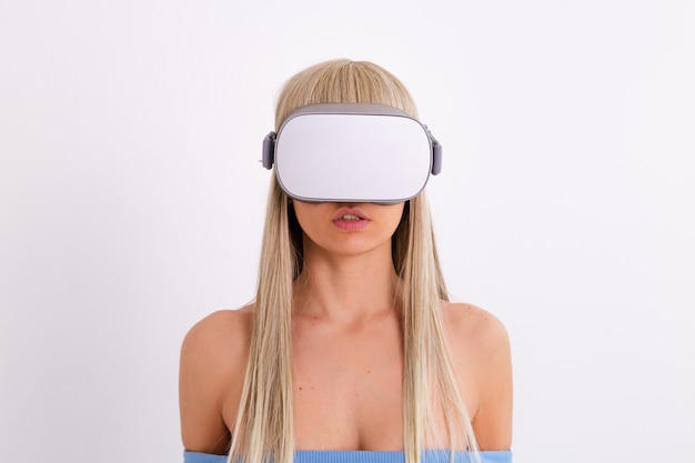 Studio photo of a young attractive woman in a warm blue fashionable suit wearing virtual reality glasses on a white