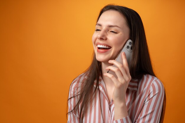 Студийное фото молодой женщины разговаривает по телефону на желтом фоне