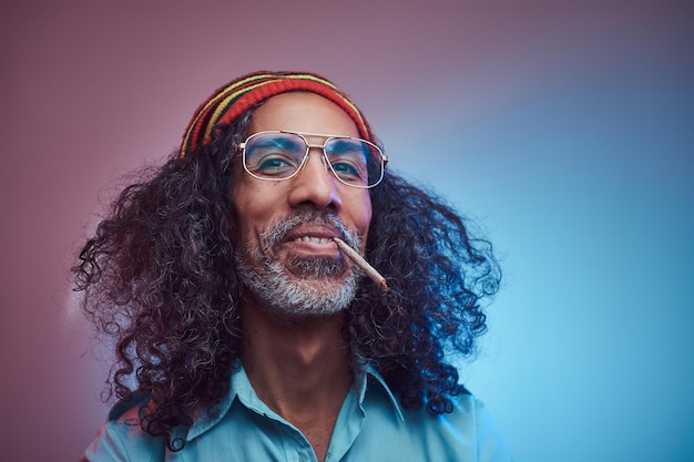 Free photo studio portrait of african rastafarian male smoking cigarettes. isolated on a blue background.