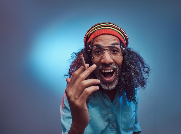 Studio portrait of African Rastafarian male smoking cigarettes. Isolated on a blue background.