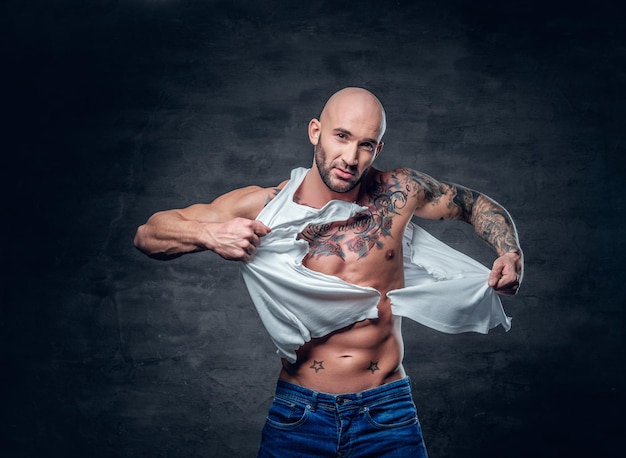 Студийный портрет спортивного мужчины с татуировкой на груди, разрывающей футболку.