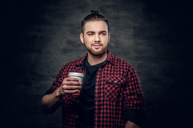 Studio portrait of bearded hipster male dressed in a fleece shirt holds coffee paper cup.