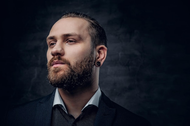 Studio portrait of bearded male dressed in a blue jacket over grey vignette background.