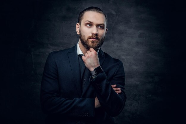 Studio portrait of bearded male dressed in a blue jacket over grey vignette background.