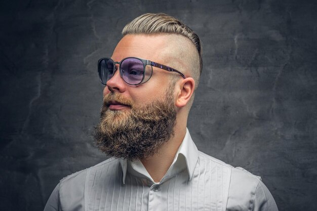 Studio portrait of bearded male with punk hairstyle dresses in a white shirt and violet sunglasses on grey vignette background.