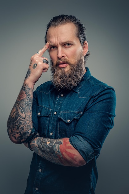 Free photo studio portrait of bearded male with tattoos on his arms, dressed in a denim shirt isolated on grey vignette background.