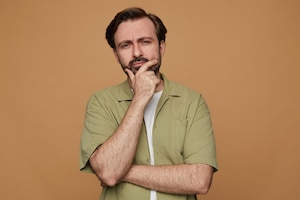 Studio portrait of bearded man posing over beige background angry and thoughtfully looking into camera