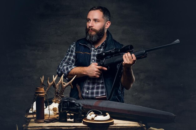 Studio portrait of a bearded modern hunter with his trophy holds a rifle.