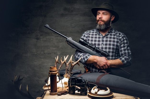 Ritratto in studio di un cacciatore tradizionale barbuto con il suo trofeo tiene un fucile.