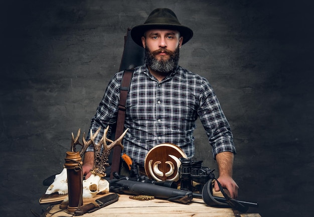 Ritratto in studio di un cacciatore tradizionale barbuto con il suo trofeo tiene un fucile.