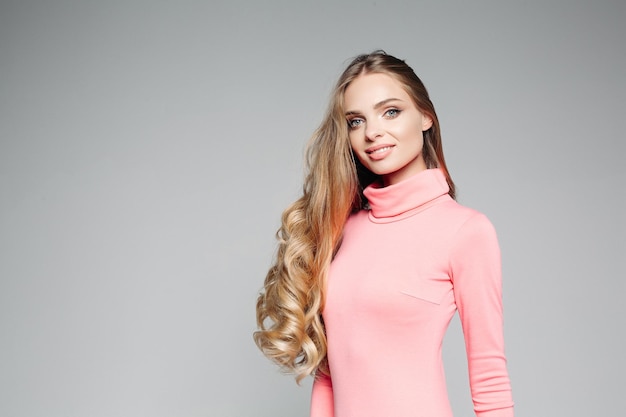 Studio portrait of a beautiful business woman blond with blue eyes with long hair wears an elegant pink dress and holds her hand on the waist Studio Isolated on a gray background