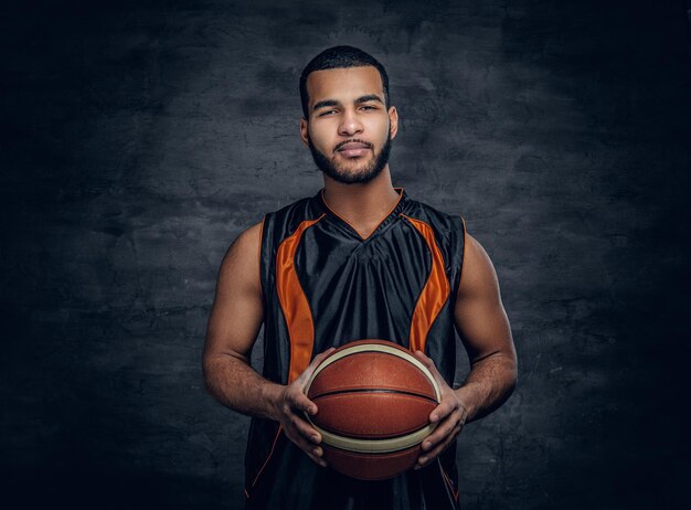 Studio portrait of Black basketball player holds a ball over grey background.