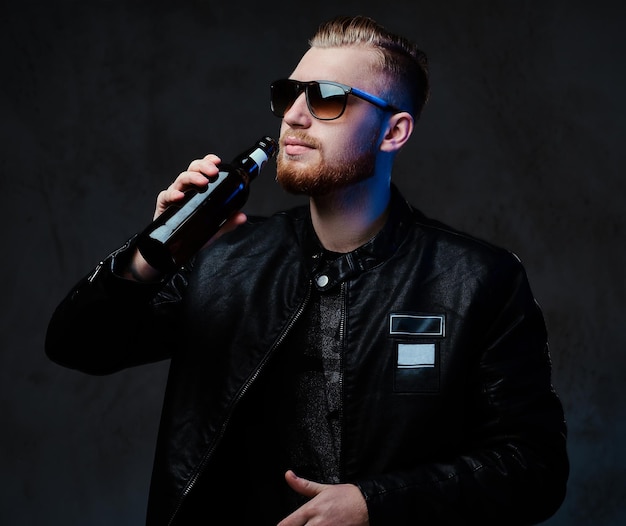 Free photo studio portrait of blond bearded stylish male holds a bottle with craft beer.