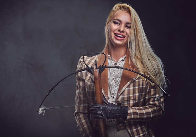 Free photo studio portrait of blond old fashioned female holds a crossbow over grey background.