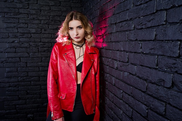 Studio portrait of blonde girl in red leather jacket against brick wall