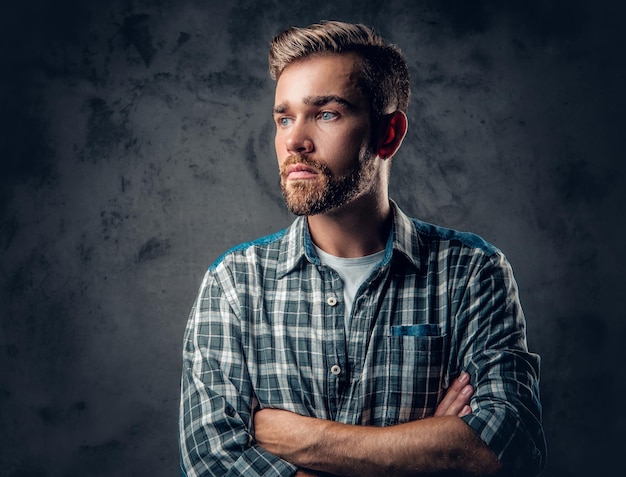 Studio portrait of a blue eyed, bearded hipster male with crossed arms over grey background.