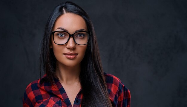 Studio portrait of brunette female in eyeglasses dressed in a red shirt over grey background.