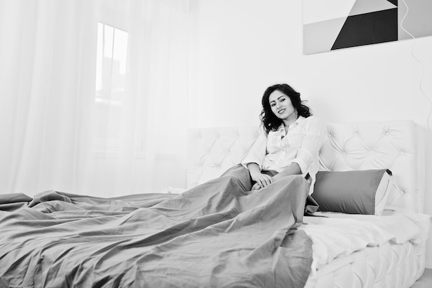 ベッドに横たわっている白いブラウスのブルネットの女の子のスタジオの肖像画
