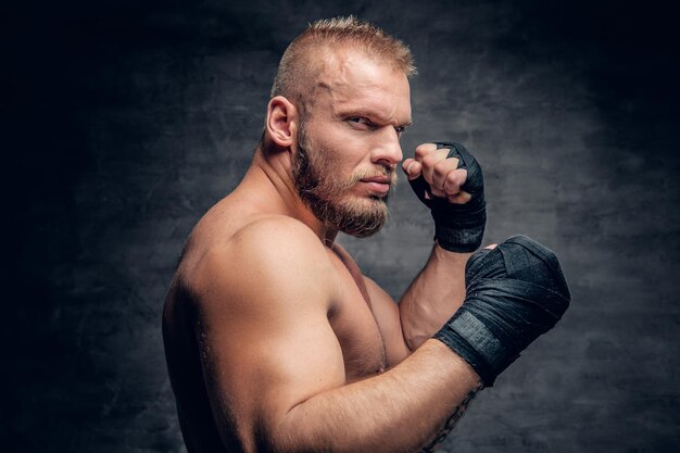 Studio portrait of brutal bearded fighter over dark grey background.