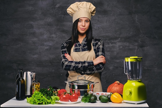 Studio portrait of chef female cook at the table with a lot of vegetables.