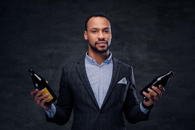 Studio portrait of elegant black American male in a suit holds beer bottles.