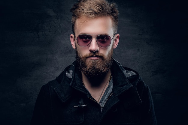 Studio portrait of fashionable bearded male in sunglasses on grey vignette background.