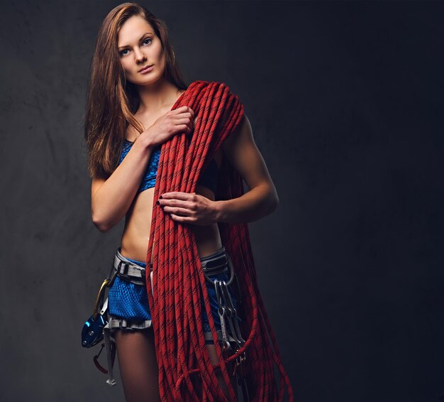 Studio portrait of female free clamber holds, climbing rope over grey background.