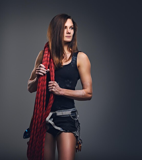 Studio portrait of female free clamber holds, climbing rope over grey background.