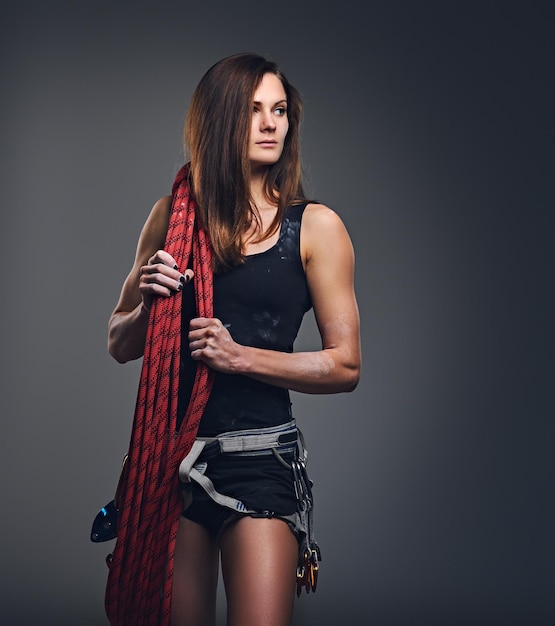 Studio portrait of female free clamber holds, climbing rope over grey background.