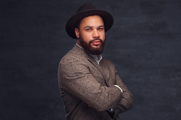 Free photo studio portrait of handsome afro-american male in an elegant brown jacket and hat. isolated on a dark background.