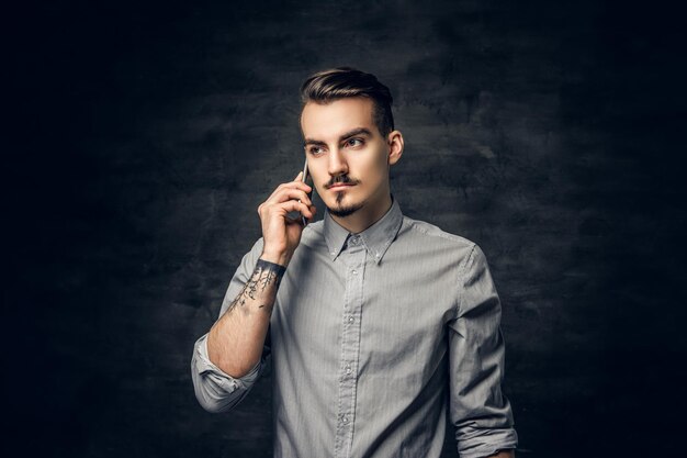 Studio portrait of handsome bearded hipster male with a tattoo on his arm talks on a smartphone.