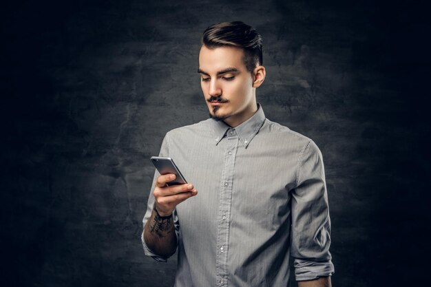 Studio portrait of handsome bearded hipster male with a tattoo on his arm using a smartphone.